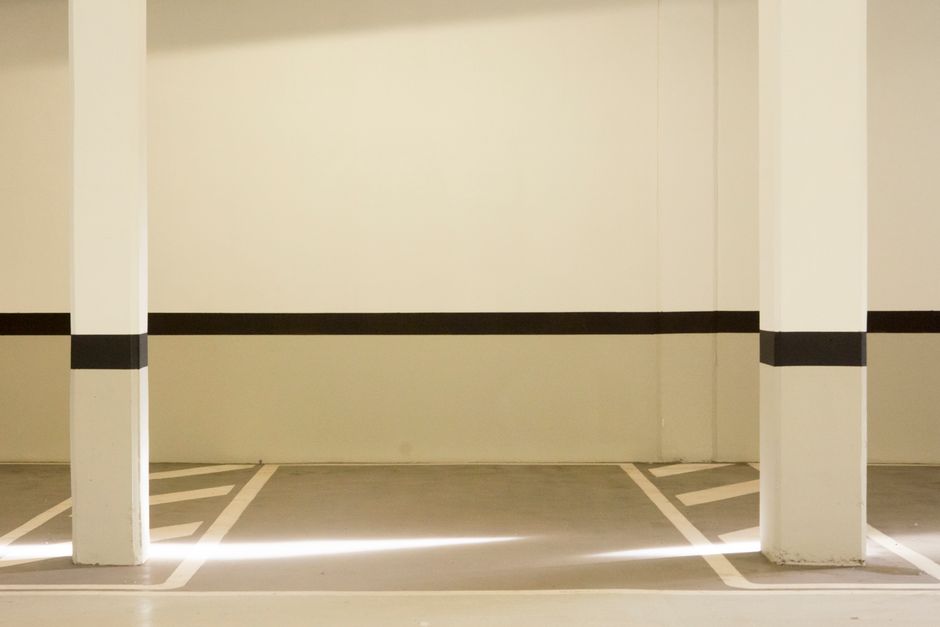 A minimalist view of a well-lit, empty parking garage interior featuring structural posts.