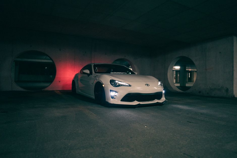A white sports car parked stylishly in a dimly lit urban garage setting.